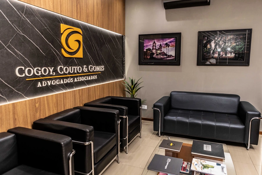 Recepção do CCG com sofás e poltronas pretas, mesa de centro com revistas e quadros fotográficos nas paredes.