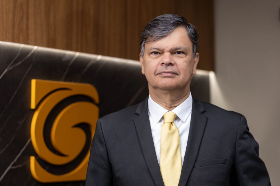 Retrato de Carlos Cogoy em frente ao logotipo da banca Cogoy, Couto & Gomes.