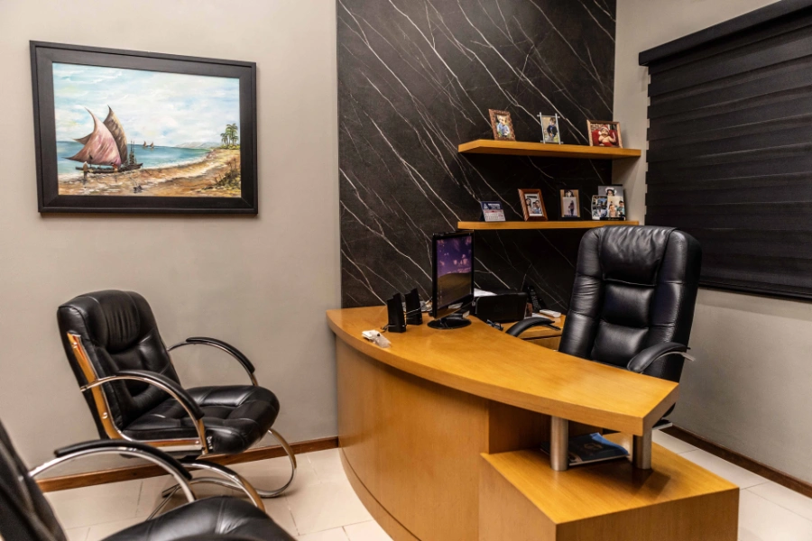 Escritório de Carlos Gomes com mesa de madeira curva, parede com prateleiras e fotos pessoais, além de quadro náutico decorativo na parede.