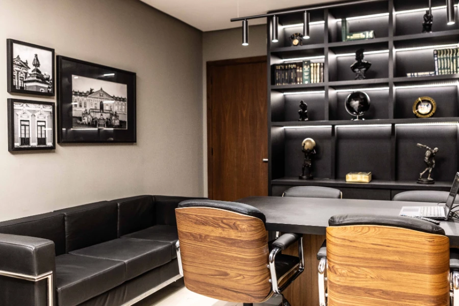 Sala de reuniões com estante iluminada, esculturas decorativas e quadros em preto e branco nas paredes laterais.